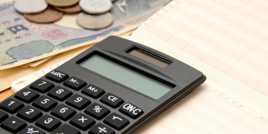 貯金や家計簿の計算、資産運用をイメージさせる、電卓と預金通帳、日本円（現金）のクローズアップ写真。