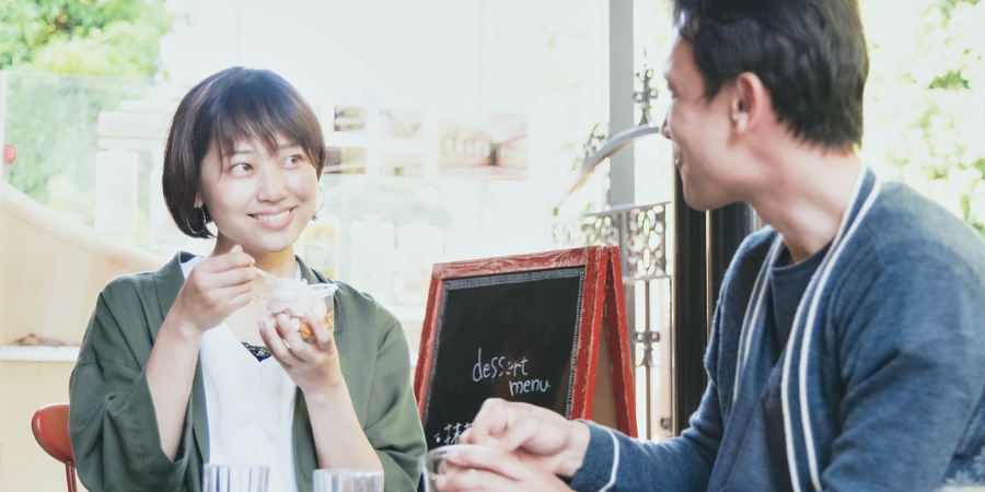 カフェでおしゃれなスイーツを楽しみながら、会話を弾ませる初々しいデート中の男女。